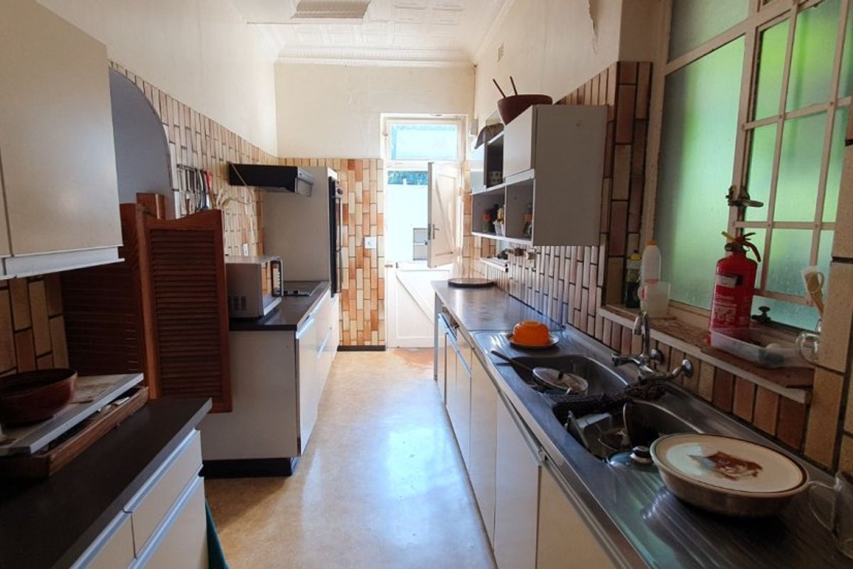A dated galley-style kitchen featuring original tiled splashbacks, built-in cabinetry, and a stainless steel sink, offering significant potential for a modern renovation.