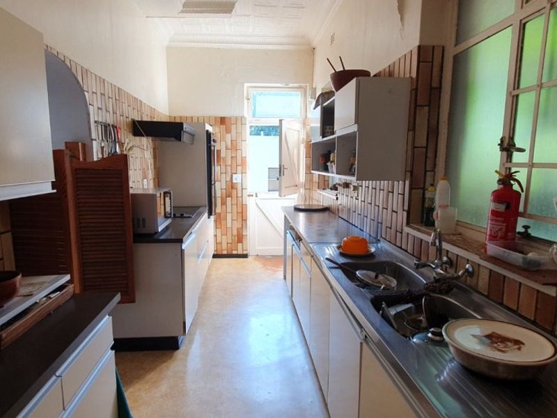 A dated galley-style kitchen featuring original tiled splashbacks, built-in cabinetry, and a stainless steel sink, offering significant potential for a modern renovation.