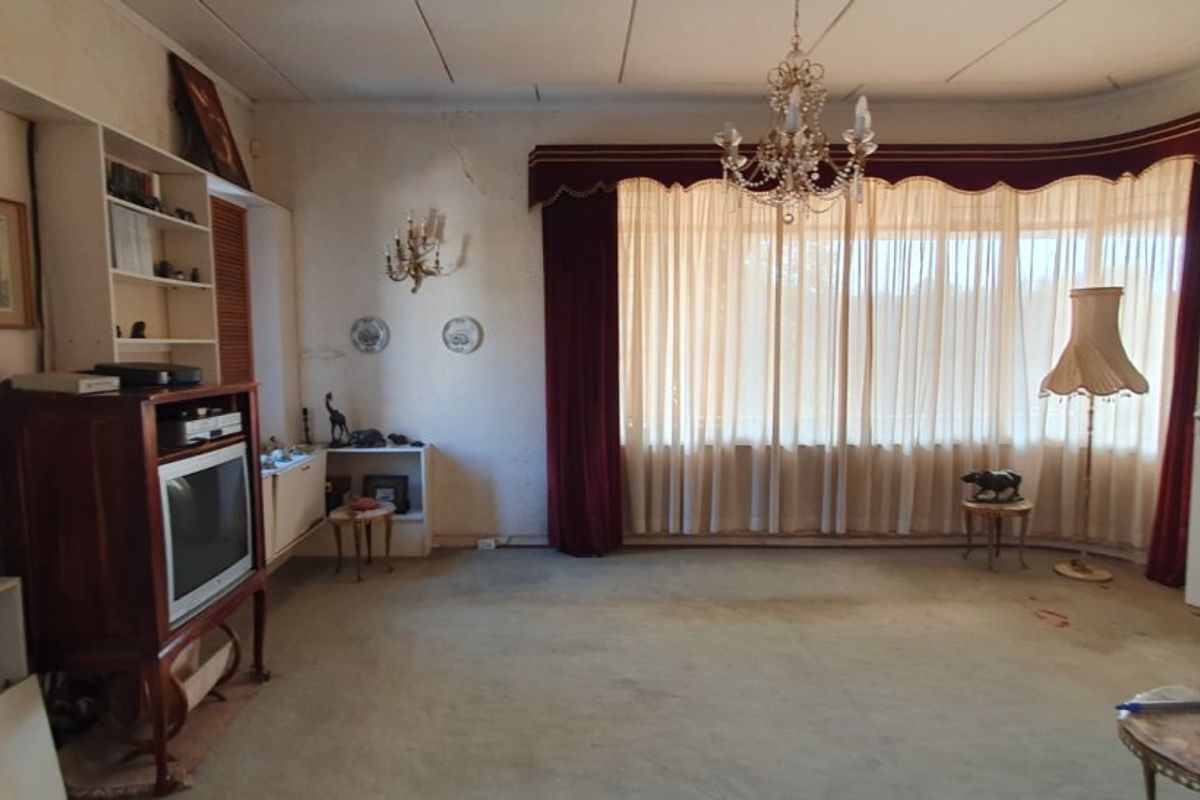 Spacious living room featuring built-in shelving, a classic chandelier, and large windows with heavy drapery, requiring cosmetic updates and wall repairs.