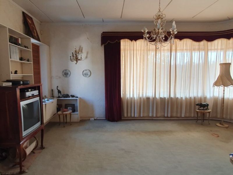 Spacious living room featuring built-in shelving, a classic chandelier, and large windows with heavy drapery, requiring cosmetic updates and wall repairs.