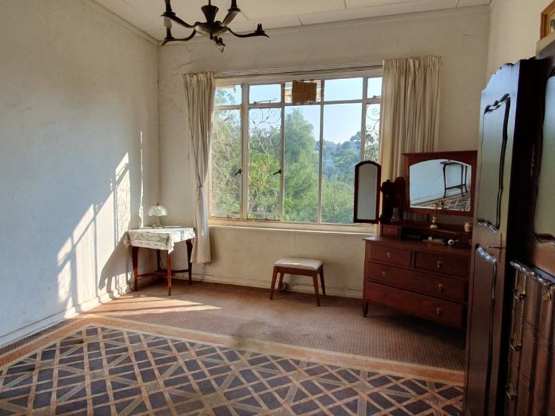 A bedroom featuring a large multi-pane window, patterned carpet flooring, and visible wall cracks, offering potential for renovation and modernization.