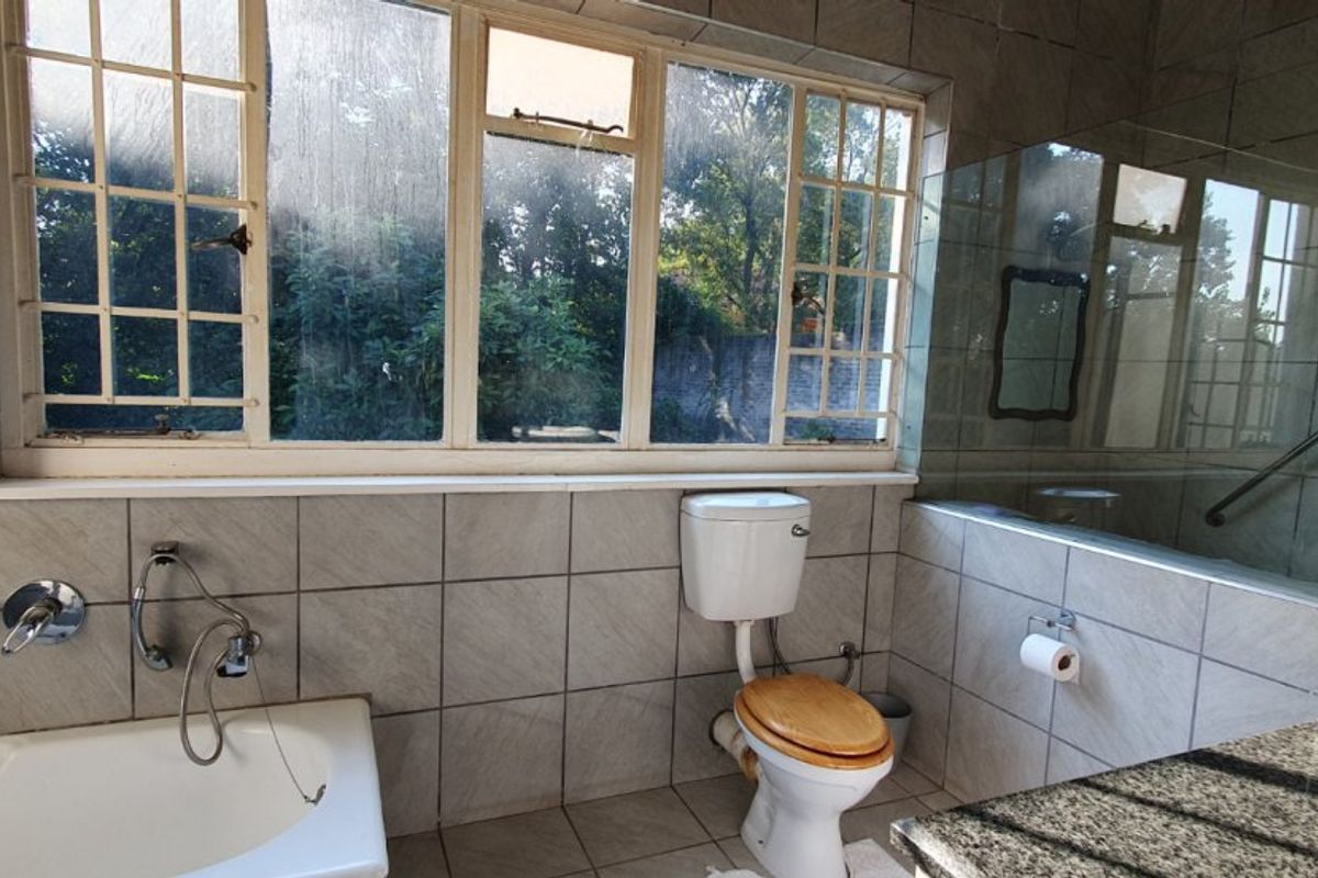 A functional bathroom featuring a bathtub, toilet, vanity with granite countertop, and a glass shower screen, with large windows providing natural light.