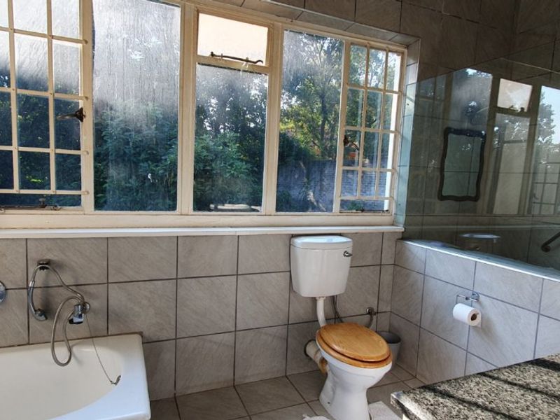 A functional bathroom featuring a bathtub, toilet, vanity with granite countertop, and a glass shower screen, with large windows providing natural light.