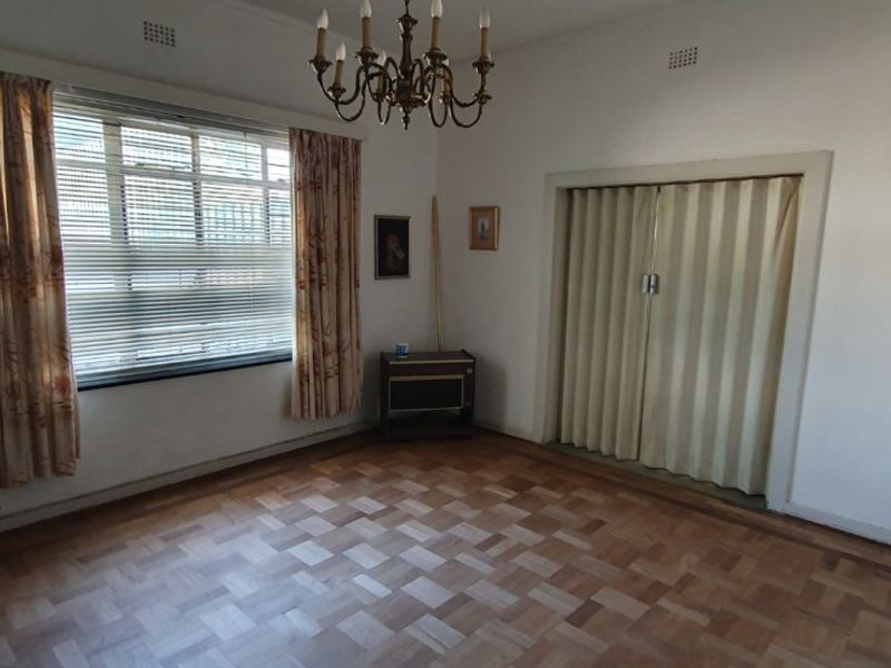 A spacious living room featuring original parquet flooring, a large window with natural light, and a folding room divider.