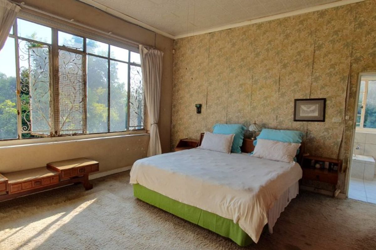 Spacious bedroom featuring large steel-framed windows, patterned wallpaper, and direct access to an en-suite bathroom. The room requires cosmetic updates to modernize the finishes.