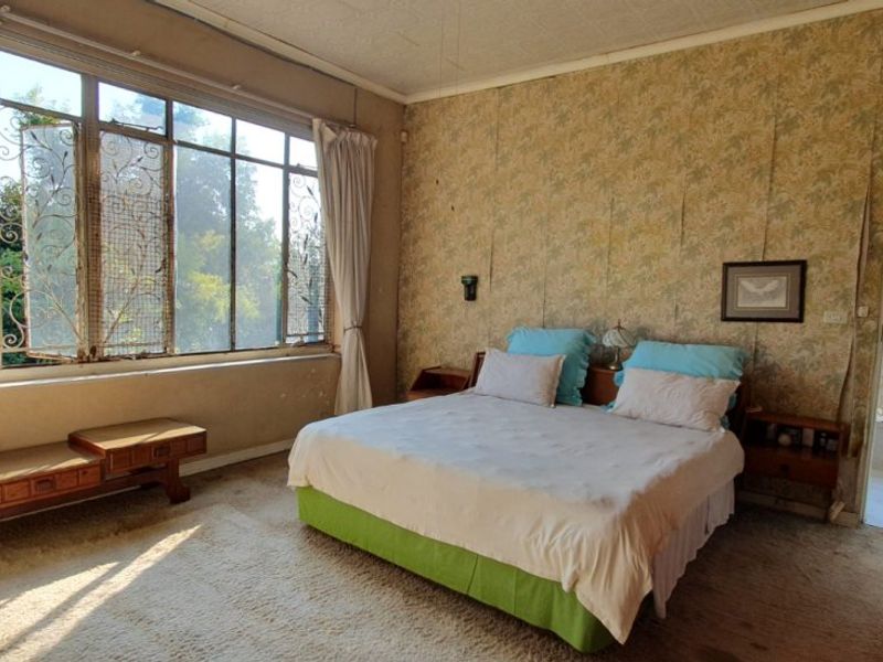 Spacious bedroom featuring large steel-framed windows, patterned wallpaper, and direct access to an en-suite bathroom. The room requires cosmetic updates to modernize the finishes.