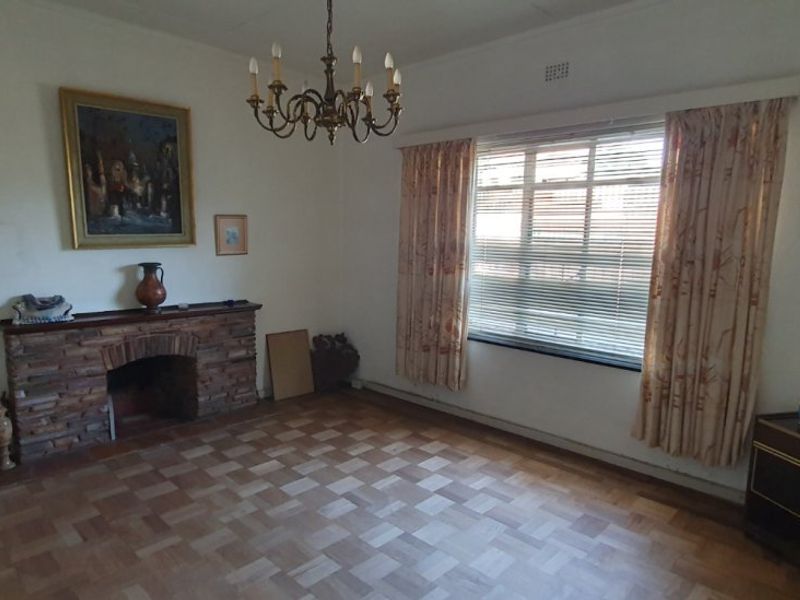 A living room featuring a stone fireplace, parquet flooring, and a classic chandelier, offering a traditional layout with potential for modernization.