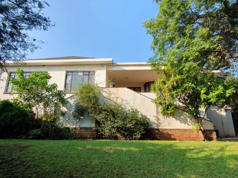 Rear view of the house featuring a covered patio, elevated staircase, and established garden area with brick foundation detailing.