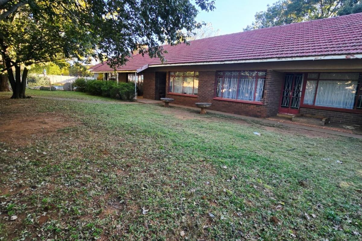A rear view of a brick house featuring a tiled roof, security gates, and a spacious garden area.