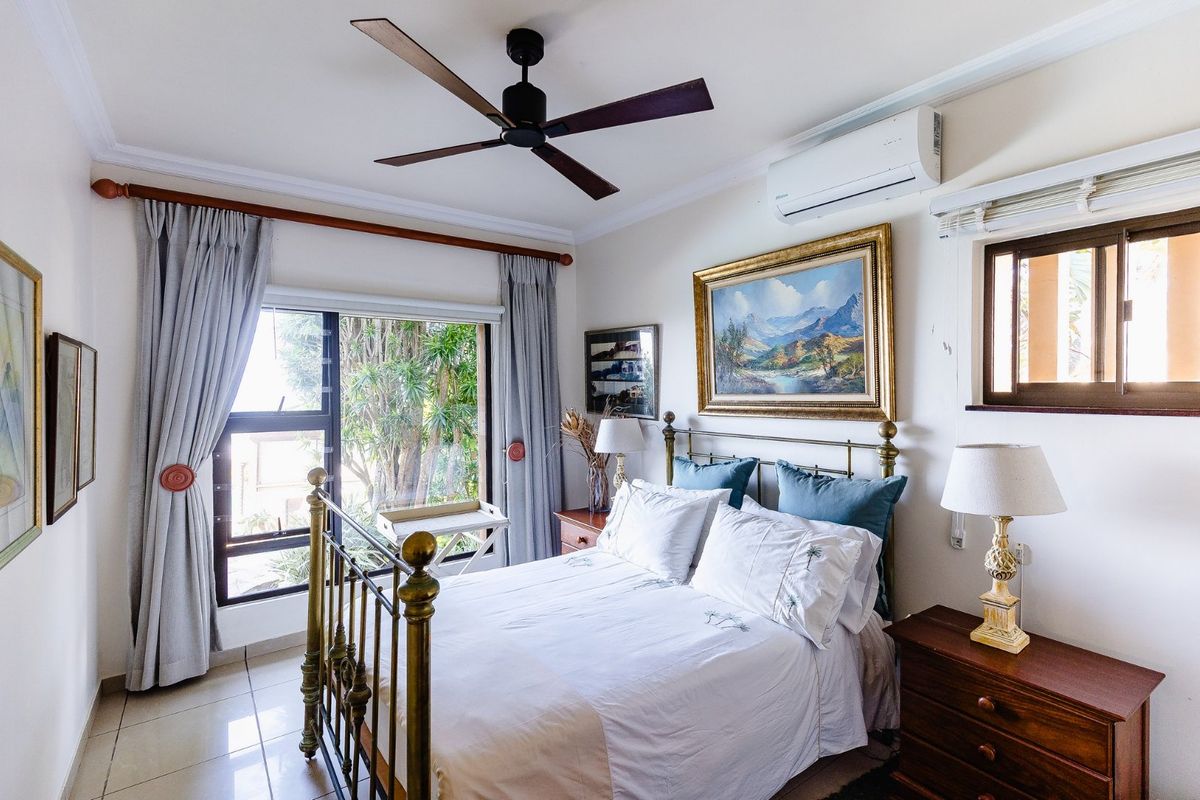 A well-maintained bedroom featuring tiled flooring, a ceiling fan, and a wall-mounted split-system air conditioner, offering a comfortable and functional living space.