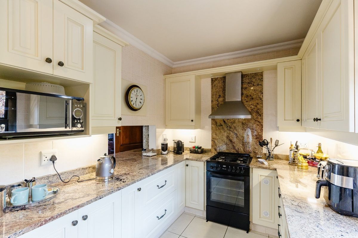 A well-maintained kitchen featuring cream cabinetry, granite countertops, a gas stove with extractor fan, and tiled finishes throughout.
