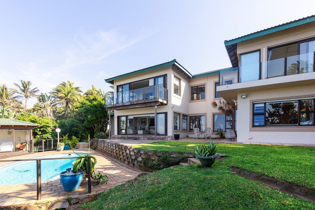Rear view of a multi-story house featuring a swimming pool, paved patio area, stone retaining wall, and glass-balustraded balconies.