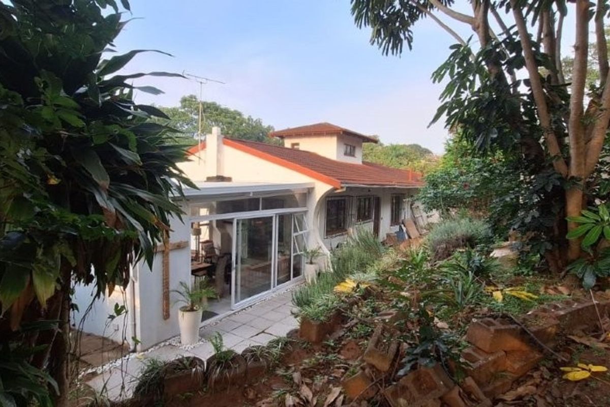 Rear view of the house featuring a tiled patio area, sliding glass doors, and a sloped garden with a retaining wall.