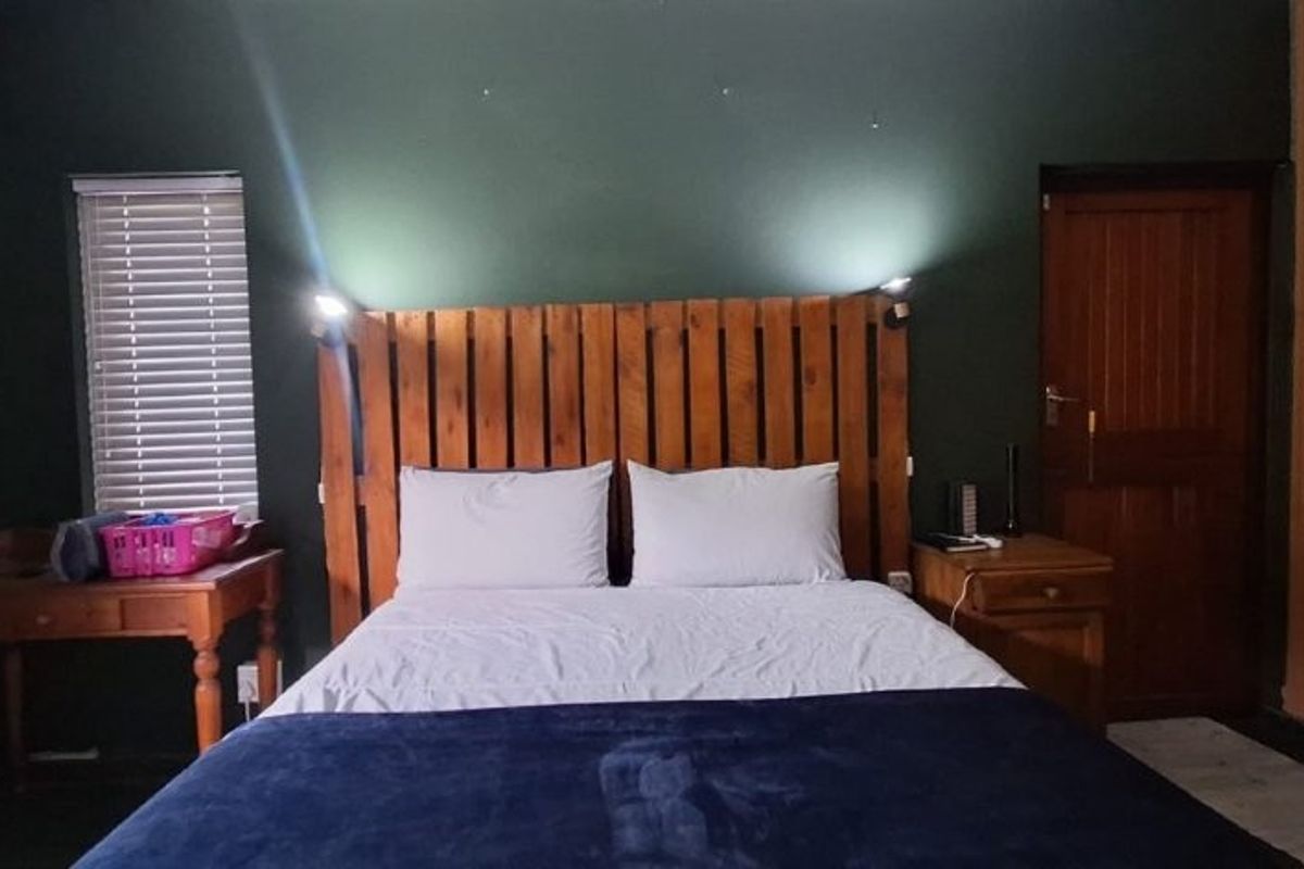 A bedroom featuring dark green walls, built-in wooden cupboards, and venetian blinds, providing a cozy and functional sleeping space.