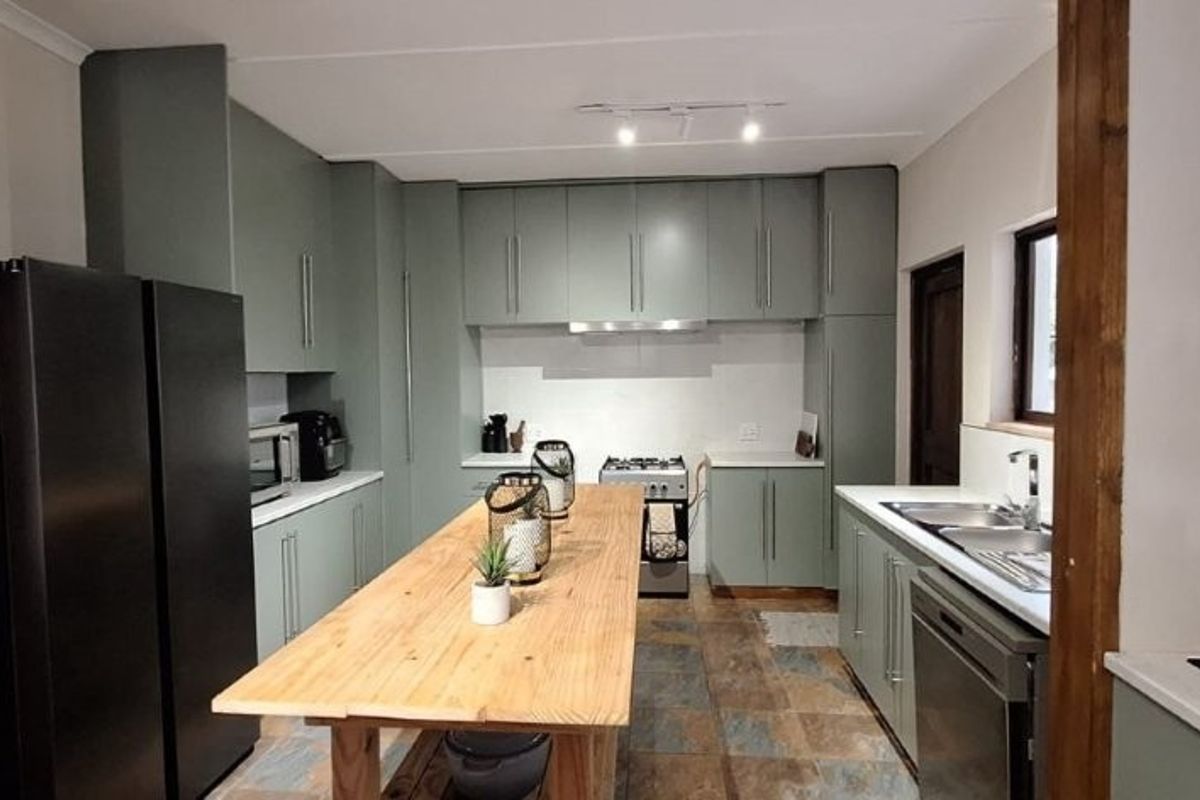 Modern kitchen featuring sage green cabinetry, stone countertops, a central wooden island, and integrated stainless steel appliances.