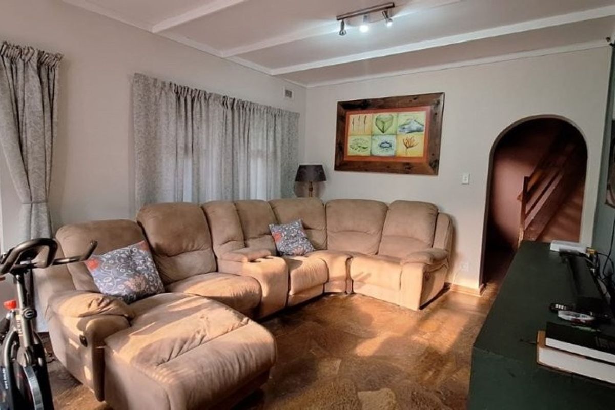 A cozy living room featuring parquet flooring, an exposed beam ceiling, and a distinctive arched doorway leading to an adjacent area.