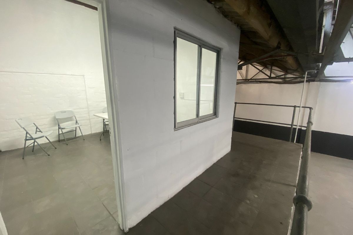 Industrial office space featuring exposed timber roof trusses, tiled flooring, and a partitioned room with a sliding window.