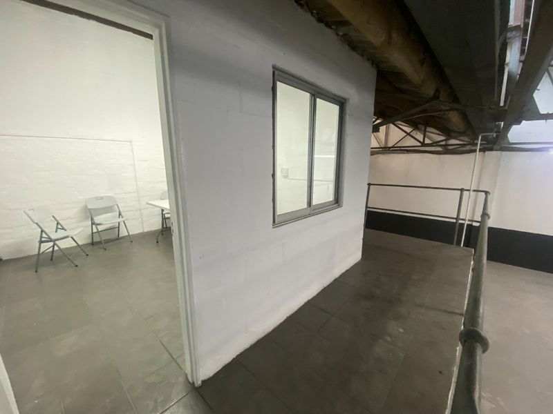 Industrial office space featuring exposed timber roof trusses, tiled flooring, and a partitioned room with a sliding window.