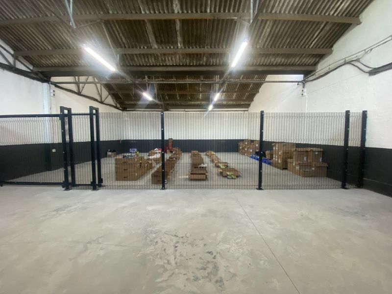 Industrial warehouse space featuring exposed timber roof trusses, concrete flooring, and secure internal mesh fencing partitions.