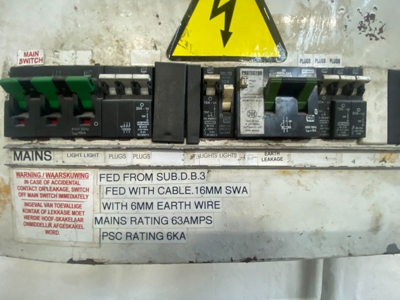 Industrial electrical distribution board featuring multiple circuit breakers, earth leakage protection, and main switch, showing signs of age and surface wear.