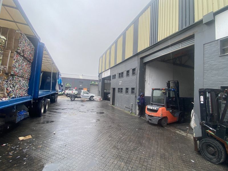 Industrial warehouse exterior featuring paved loading area, roller shutter access, and corrugated metal cladding, suitable for logistics or manufacturing operations.