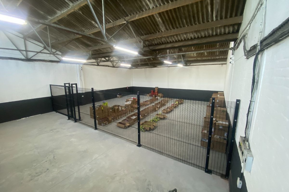 Spacious industrial utility area featuring high ceilings with exposed steel trusses, concrete flooring, and secure internal fencing.