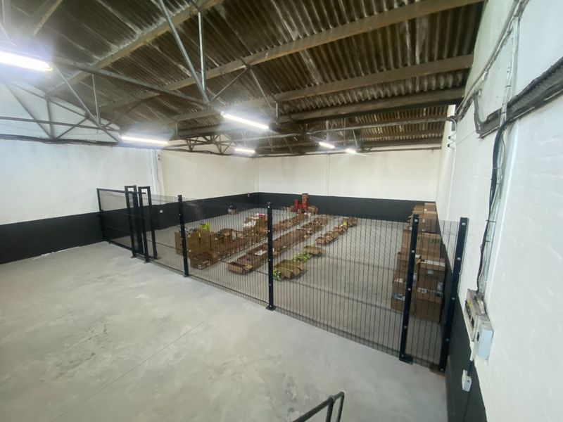 Spacious industrial utility area featuring high ceilings with exposed steel trusses, concrete flooring, and secure internal fencing.