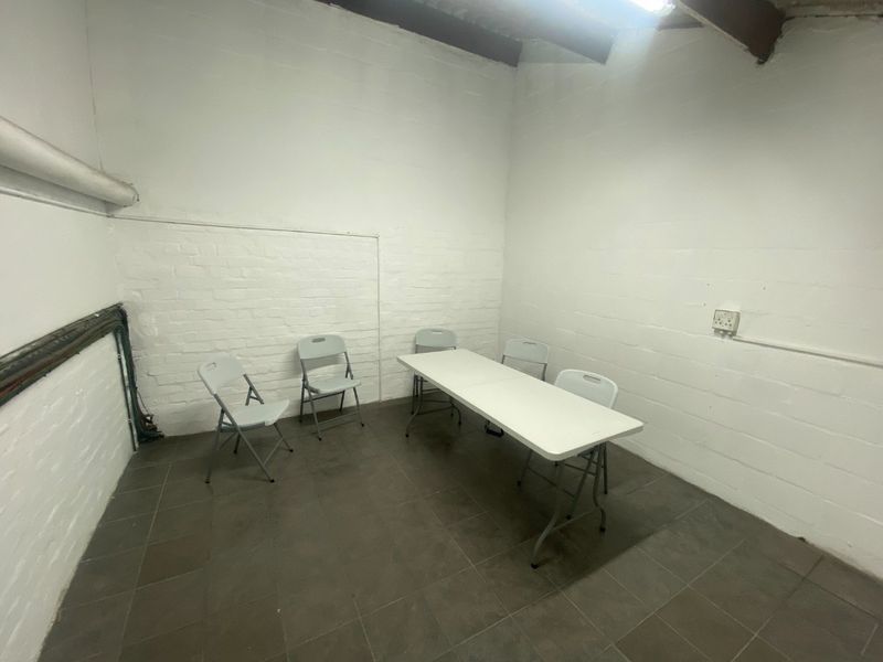 A functional industrial-style office space featuring painted brick walls, tiled flooring, and exposed ceiling beams, suitable for a variety of commercial uses.