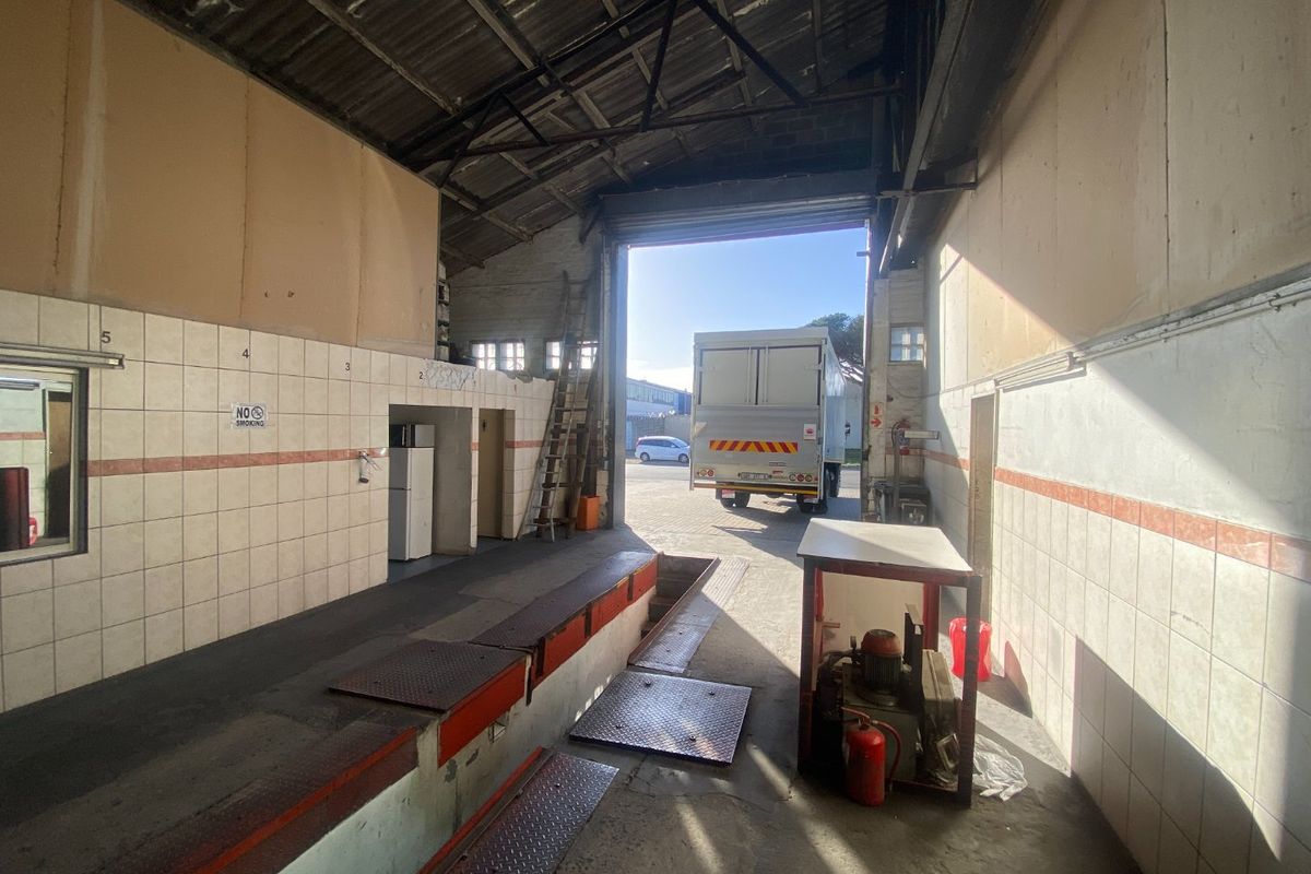 Industrial garage space featuring a vehicle inspection pit, high ceilings with exposed trusses, and large roller shutter door access.