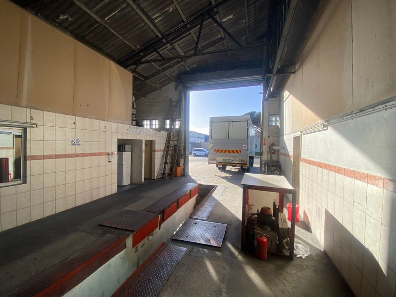 Industrial garage space featuring a vehicle inspection pit, high ceilings with exposed trusses, and large roller shutter door access.