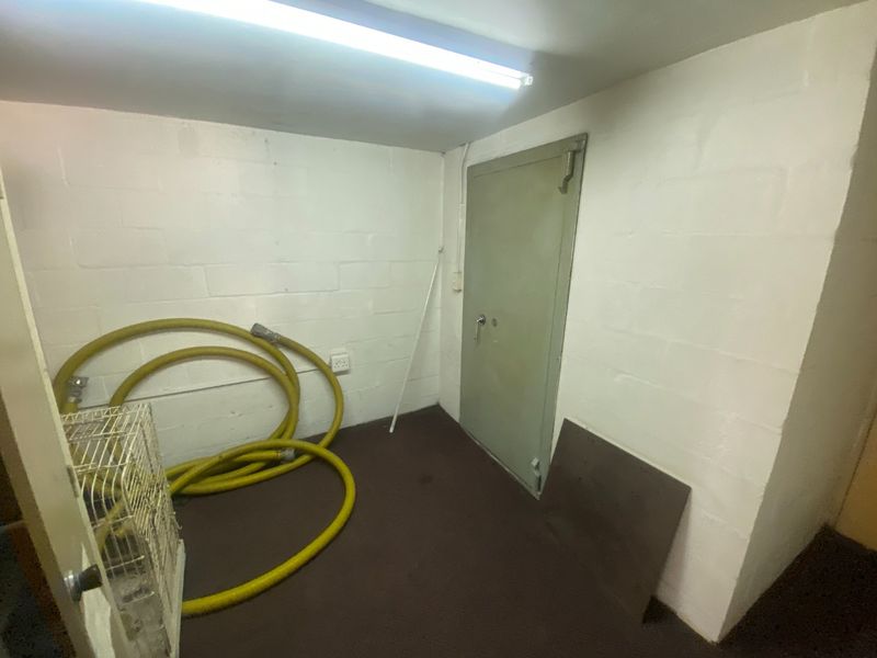 A functional utility space featuring masonry block walls, a heavy-duty steel door, and overhead fluorescent lighting, suitable for storage or industrial use.