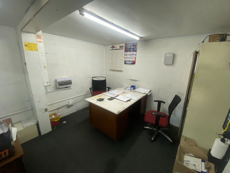 A functional industrial office space featuring exposed blockwork walls, basic fluorescent lighting, and visible electrical infrastructure.