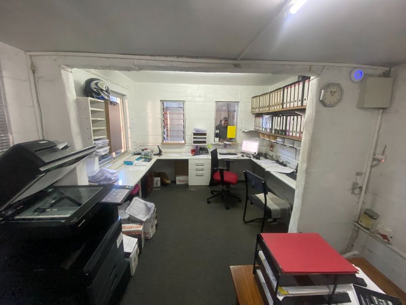 Functional industrial office space featuring built-in desk workstations, integrated shelving units, and louver windows for ventilation.
