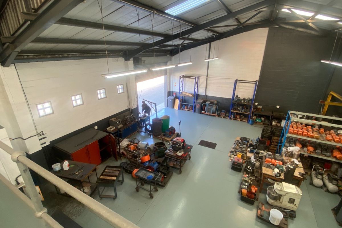 Spacious industrial utility area featuring high ceilings with exposed steel trusses, epoxy flooring, and a large roller shutter door for easy access.