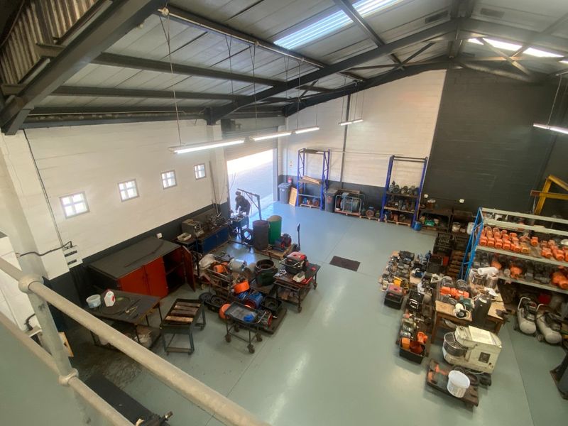 Spacious industrial utility area featuring high ceilings with exposed steel trusses, epoxy flooring, and a large roller shutter door for easy access.