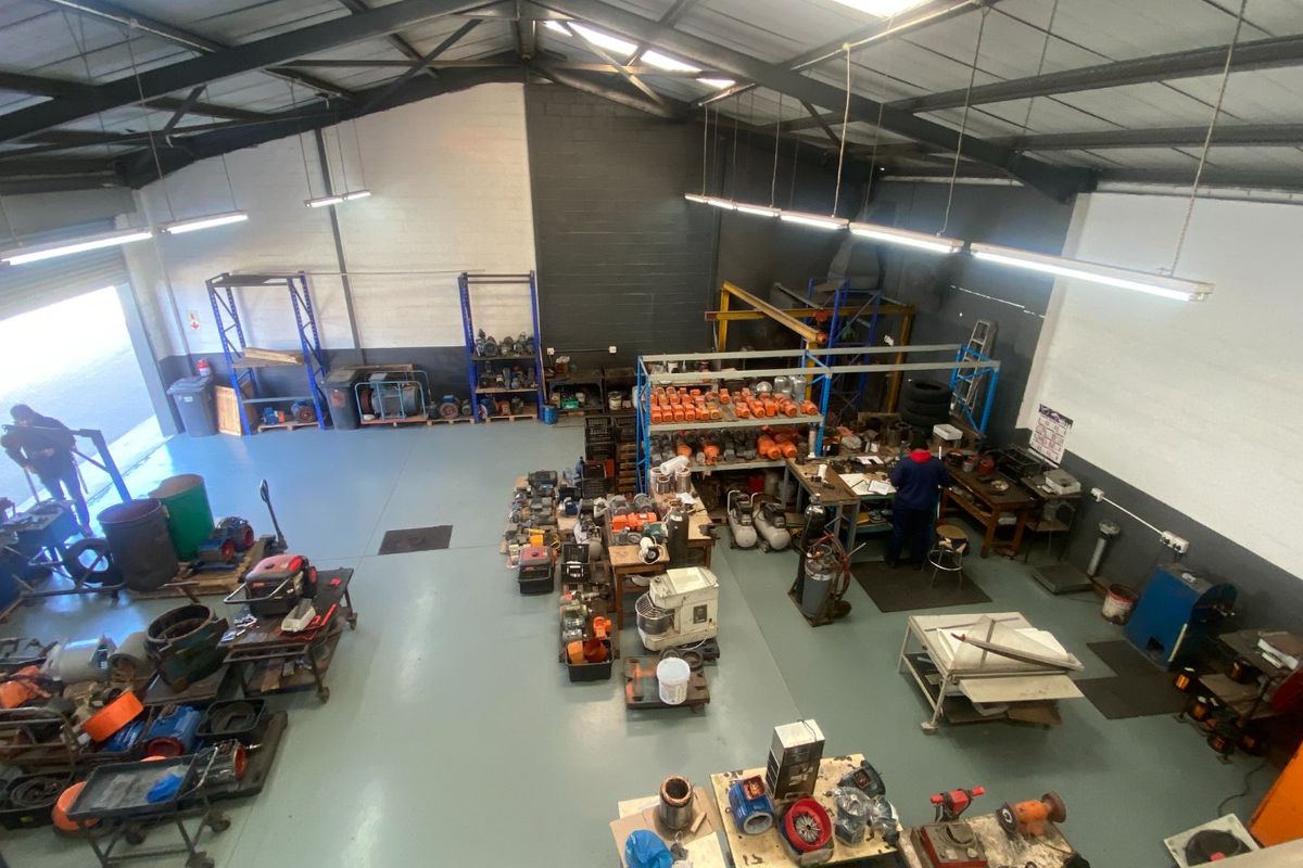 Spacious industrial workshop featuring high ceilings with exposed steel trusses, durable epoxy flooring, and integrated fluorescent lighting, suitable for manufacturing or storage operations.