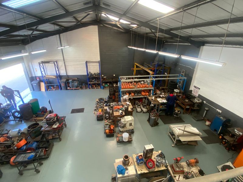 Spacious industrial workshop featuring high ceilings with exposed steel trusses, durable epoxy flooring, and integrated fluorescent lighting, suitable for manufacturing or storage operations.