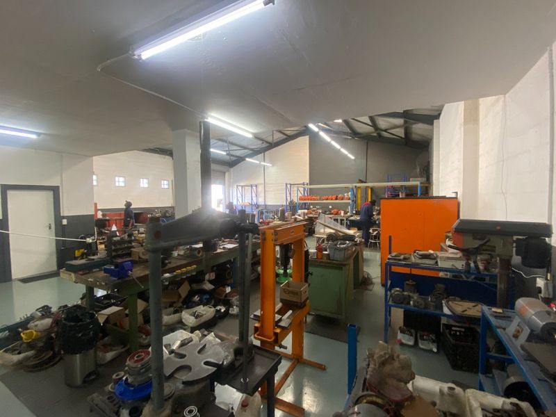 Spacious industrial workshop area featuring high ceilings with exposed steel trusses, durable epoxy flooring, and functional overhead fluorescent lighting.
