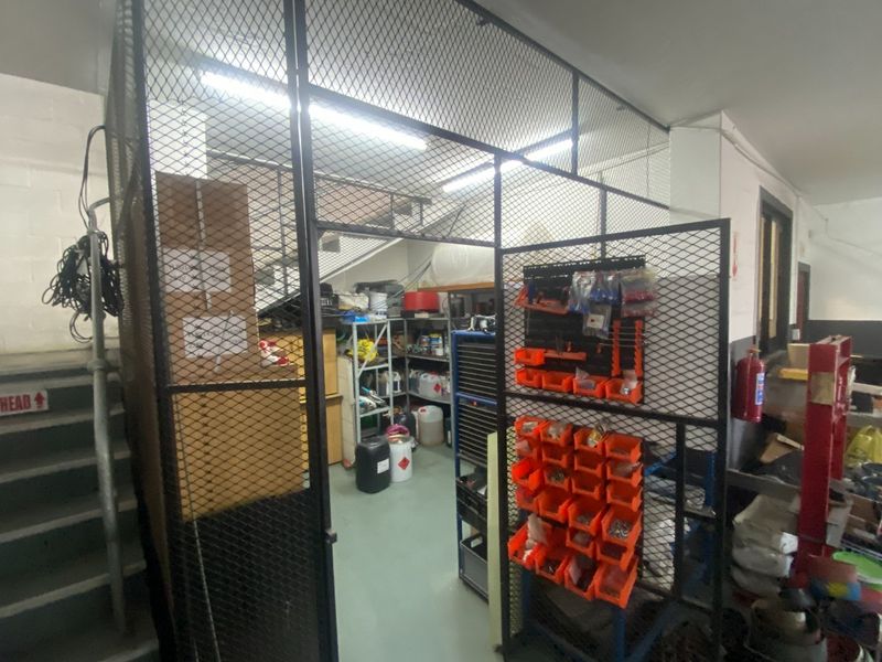 A secure industrial utility storage area enclosed by a metal mesh cage, featuring overhead fluorescent lighting and concrete flooring.