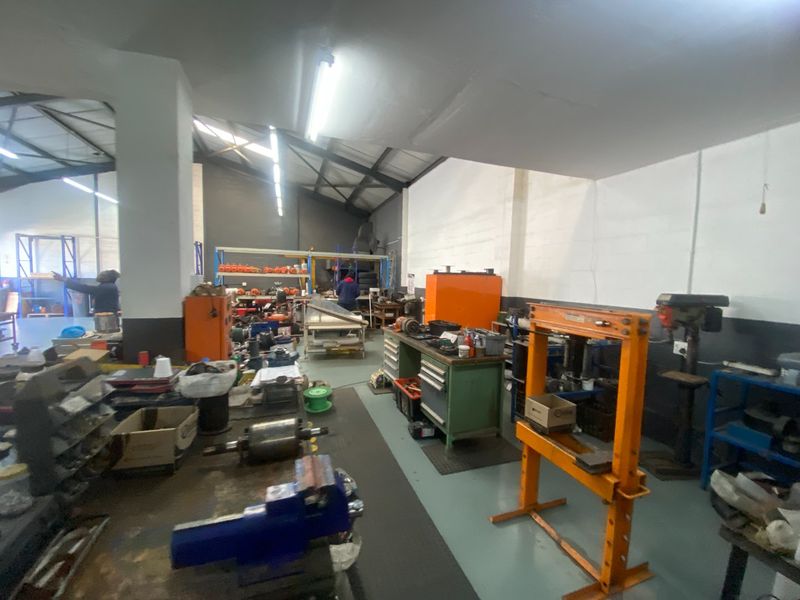 Industrial workshop space featuring high ceilings with exposed steel trusses, durable epoxy flooring, and integrated fluorescent lighting suitable for heavy-duty operations.
