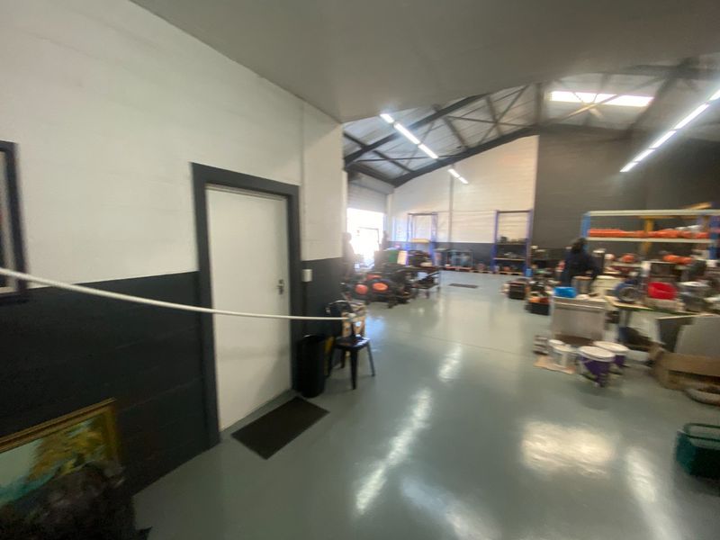 Spacious industrial utility area featuring epoxy-coated concrete flooring, exposed steel roof trusses, and high-bay fluorescent lighting, suitable for workshop or storage operations.