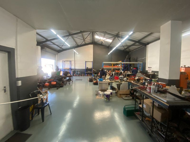 Spacious industrial workshop area featuring exposed steel roof trusses, durable epoxy flooring, and high-level fluorescent lighting, suitable for various commercial or manufacturing operations.
