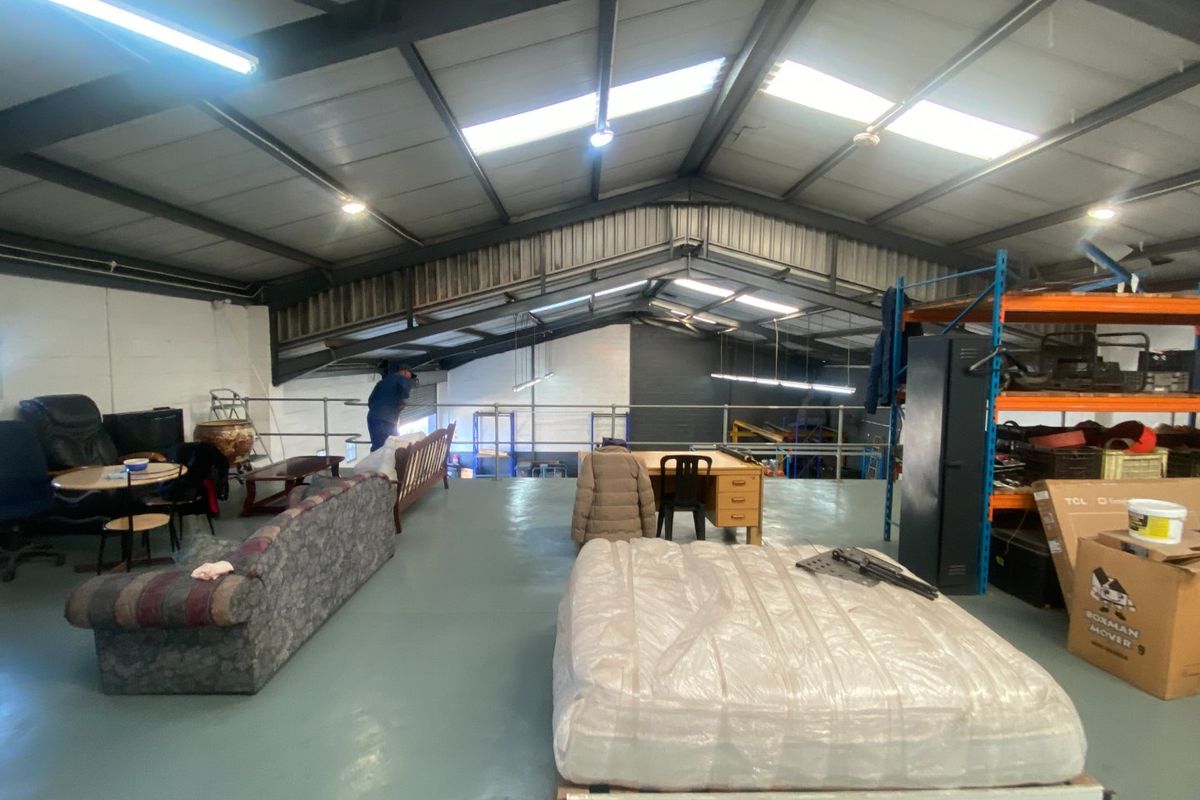 Spacious industrial mezzanine level featuring exposed steel roof trusses, skylights, and durable epoxy flooring, suitable for storage or flexible workspace use.