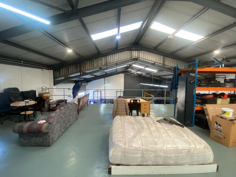 Spacious industrial mezzanine level featuring exposed steel roof trusses, skylights, and durable epoxy flooring, suitable for storage or flexible workspace use.
