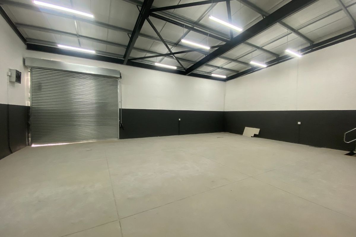 Spacious industrial utility area featuring high ceilings with exposed steel trusses, concrete flooring, and a large roller shutter door for easy access.