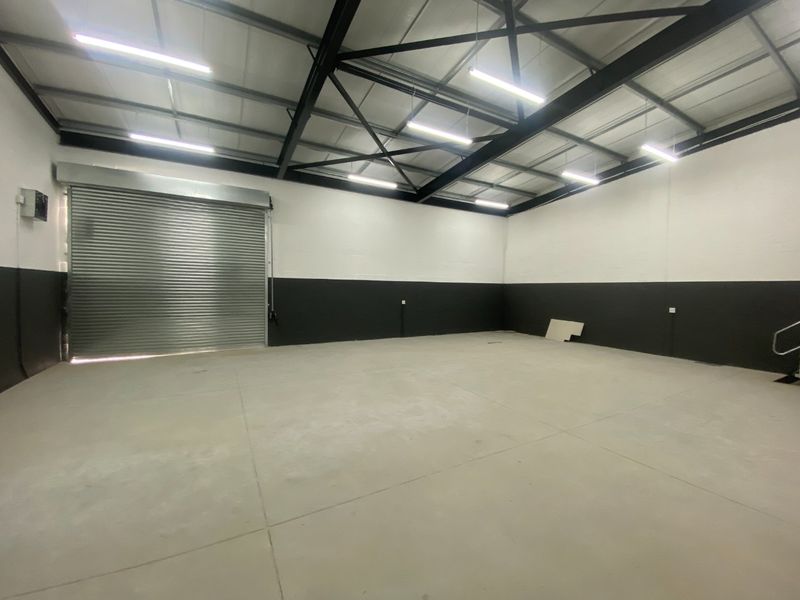 Spacious industrial utility area featuring high ceilings with exposed steel trusses, concrete flooring, and a large roller shutter door for easy access.