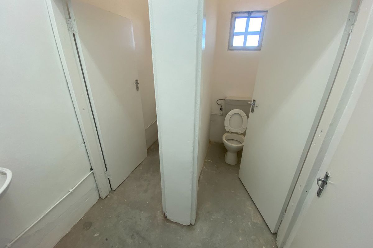 A basic industrial-style bathroom facility featuring two separate toilet cubicles with unfinished concrete flooring and simple white painted walls.