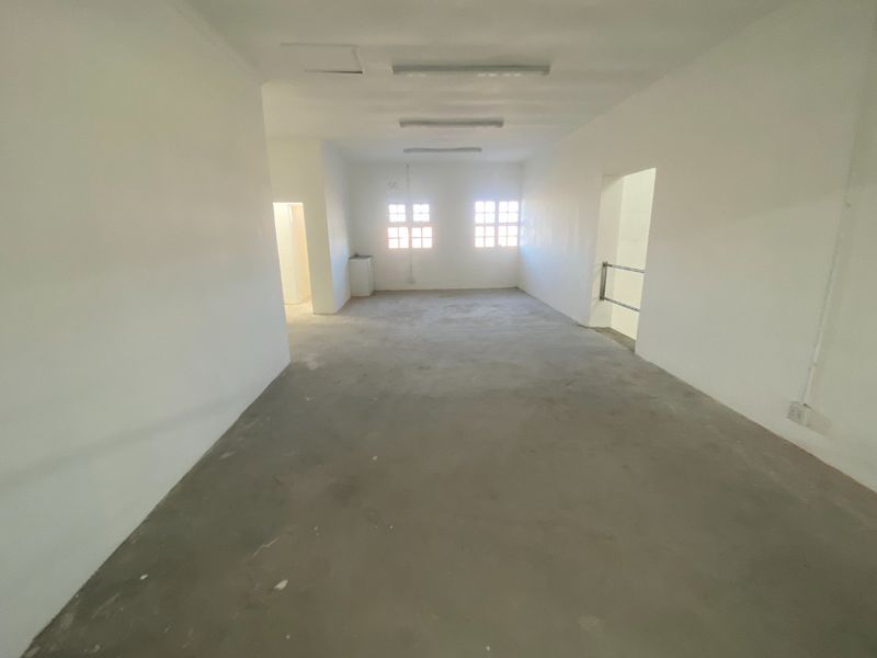 An open-plan industrial utility space featuring concrete flooring, fluorescent lighting, and multiple access points, suitable for storage or workshop use.