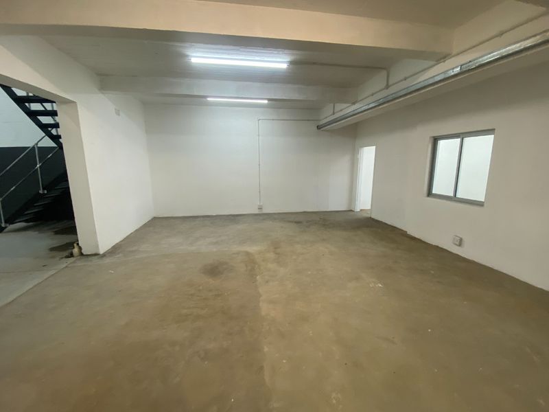 An empty industrial utility space featuring concrete flooring, exposed ceiling beams, and a metal staircase, suitable for storage or workshop use.