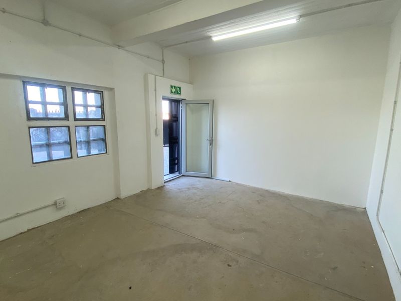An empty industrial utility space featuring concrete flooring, exposed electrical conduit, and an emergency exit door.